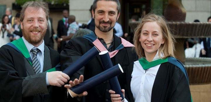 Three graduates wearing robes and holding their scrolls - two males, one female